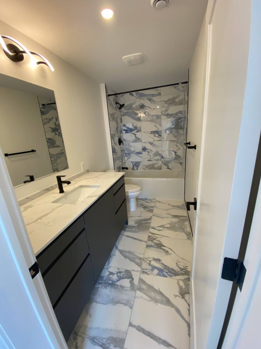 Modern bathroom with black vanity, marble tile flooring, and tub shower