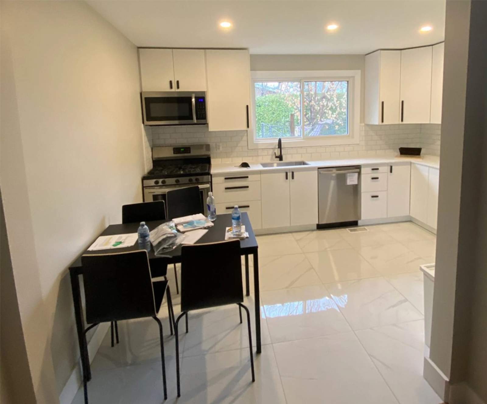 Modern kitchen renovation featuring white cabinetry, stainless steel appliances, tiled backsplash, dining area, and large window bringing in natural light.